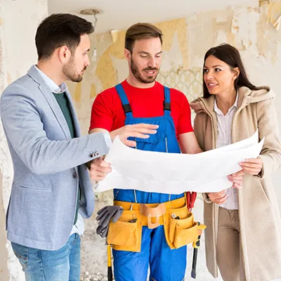 Young couple meeting with builder on-site and looking at blueprint